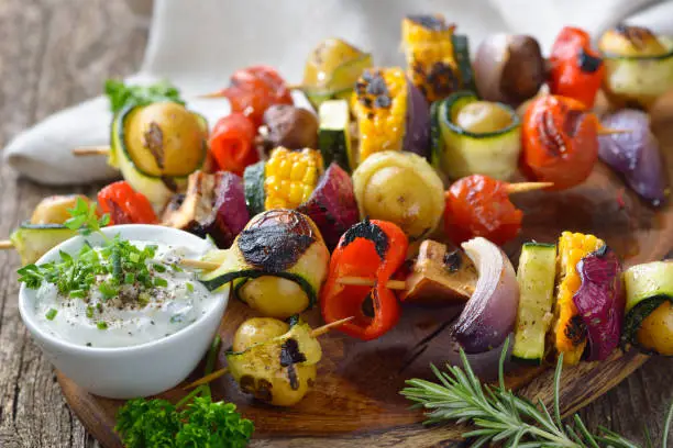 Grilled skewers with mixed vegetables served  on a wooden cutting board with a vegan herb dip