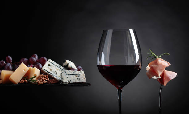 Glass of red wine with various cheeses , grapes and prosciutto .
