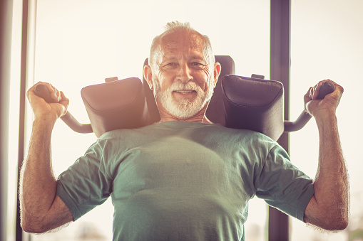 Active senior man using weights machine in the gym