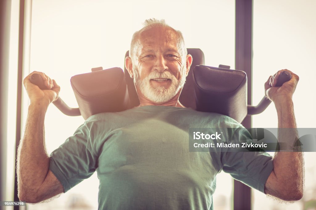 Hard exercise. Active senior man using weights machine in the gym Exercise Machine Stock Photo