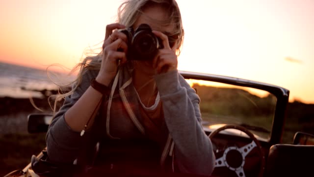 Woman on road trip sitting in convertible and taking photos