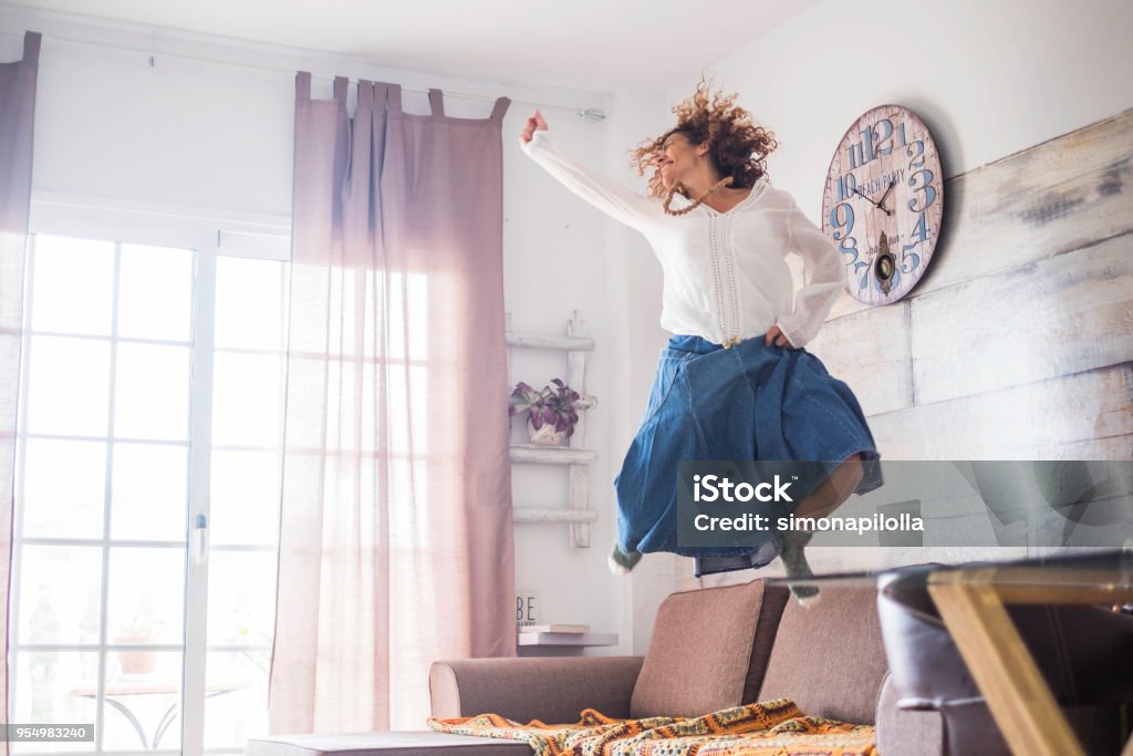 beautiful caucasian woman jump at home crazy happiness for beautiful woman jumping at home for great joy after a success or for a nice lifestyle. hippy chic bohemien clothes and bright funny image with winner concept Happiness Stock Photo