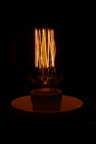 istock Glowing vintage lamp filament isolated on the dark background 954983384
