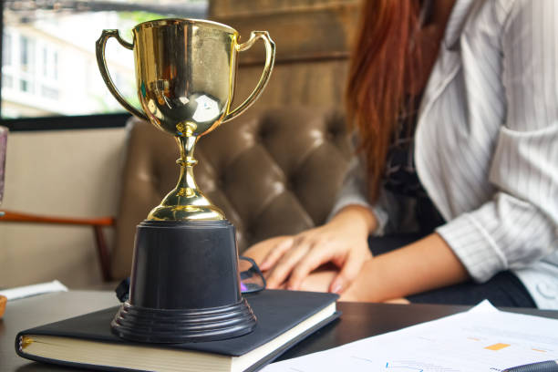 istock Trophy on working table which have document and pen and black book and bakcground working women 954983938