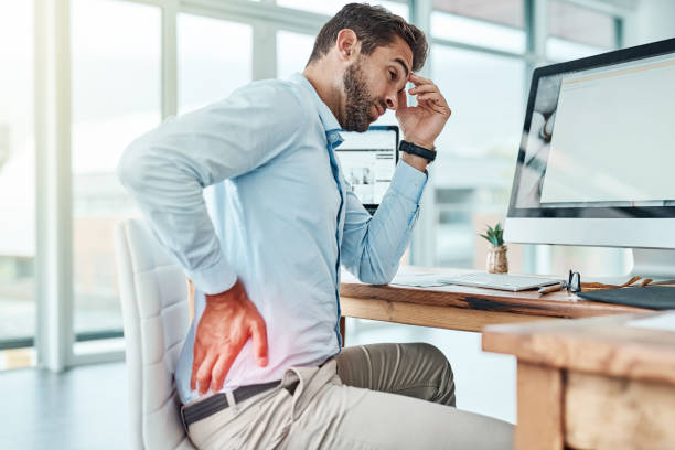 Sitting for long periods of time can strain your body Shot of a young businessman suffering with back pain while working in an office office back pain stock pictures, royalty-free photos & images