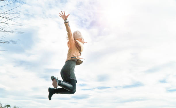 istock Jumping woman under clouds sunset outstretched arms and legs 954991796