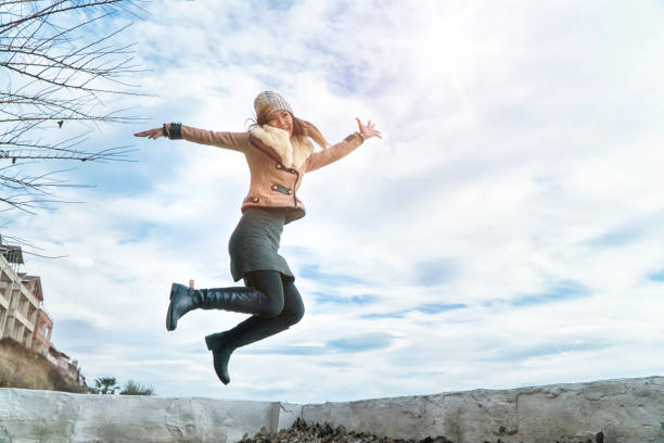istock Jumping woman under clouds sunset outstretched arms and legs 954992242