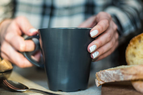 istock woman's hands with white manicure holding a mug 955014950
