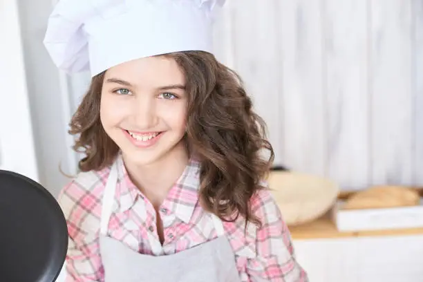 Beautiful girl. Little cook. White cap. Brown curly hair.