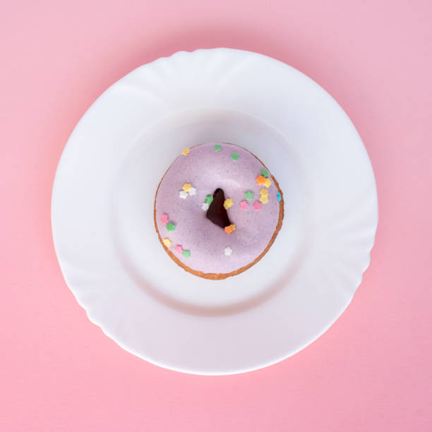 istock A donut covered in purple frosting on a white plate on a pink surface 955032180