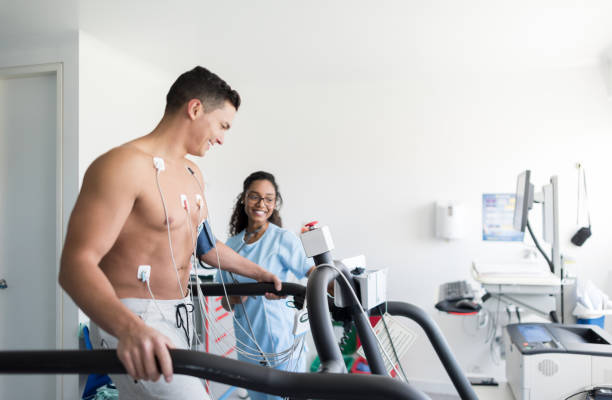 Beautiful african american nurse monitoring a cheerful male patient doing a stress test Beautiful african american nurse monitoring a cheerful male patient doing a stress test both looking very happy and smiling electrode stock pictures, royalty-free photos & images