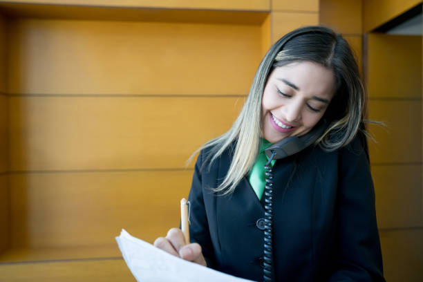 concierge latinoamericano che lavora alla reception parlando al telefono sorridendo - hotel reception paper hotel tourism foto e immagini stock