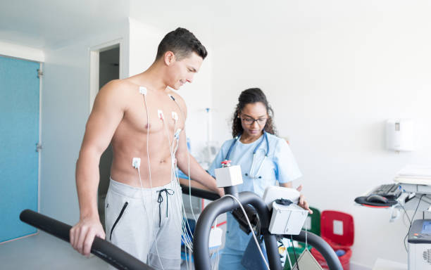 Handsome young man at the clinic doing a treadmill stress test and nurse taking his vital signs Handsome young man at the clinic doing a treadmill stress test and black nurse taking his vital signs stress test stock pictures, royalty-free photos & images