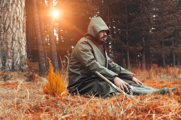 Man sitting and digging summer afternoon  in forest with long coat