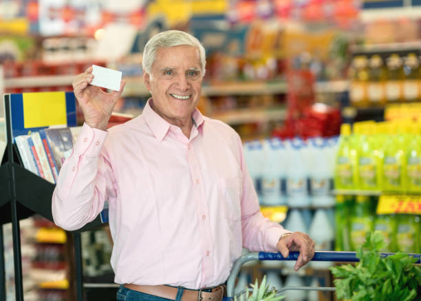 istock Senior man at a food store holding a loyalty program card and looking at camera smiling 955049978