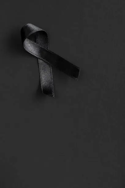 Photo of Black satin ribbon on black background. R.I.P. symbol.