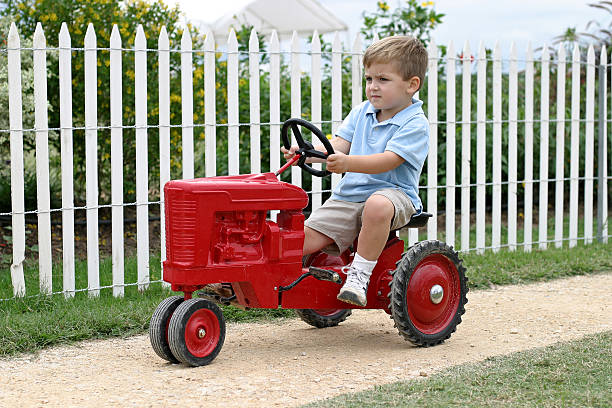 Adorable cute Asian toddler boy riding and play on an old tractor car parking in outdoor field happily. Young baby outdoor experience learning activity concept.