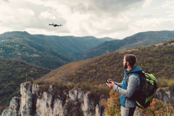 Hiker on the mountain top flying a drone to make videos and photos Tourist on the mountain flying a drone drone point of view stock pictures, royalty-free photos & images