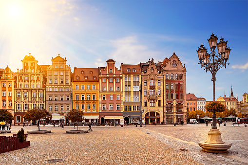 Central market square in Wroclaw Poland with old colourful houses, street lantern lamp and walking tourists people at gorgeous stunning morning sunrise sunshine. Travel vacation concept.
