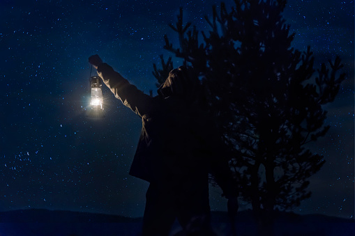 Hombre de Woodman con lámpara de gas en bosque bajo las estrellas en la noche en bosque photo