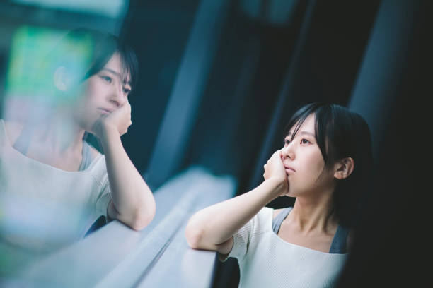 A young woman is looking outside through the window and thinking something deeply alone.