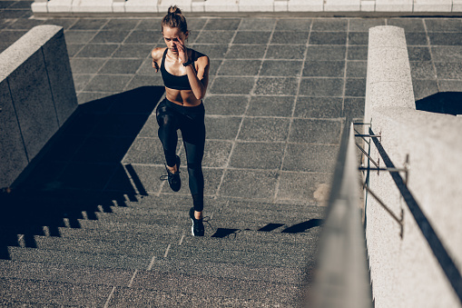 Fit sportswoman running up the steps. Female runner exercising on staircase outdoors.