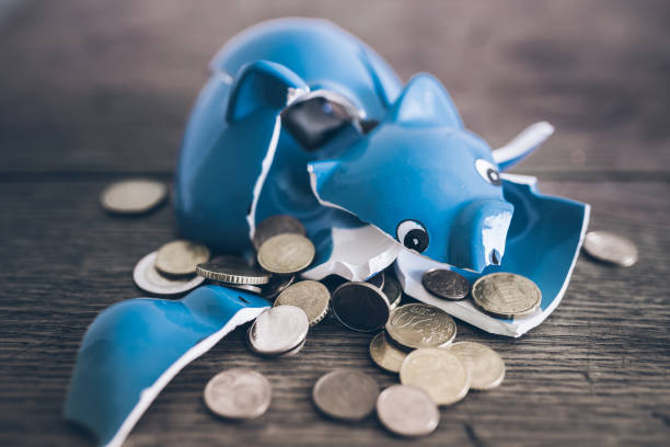 shattered broken piggy bank with coins on rustic wooden table stock photo
