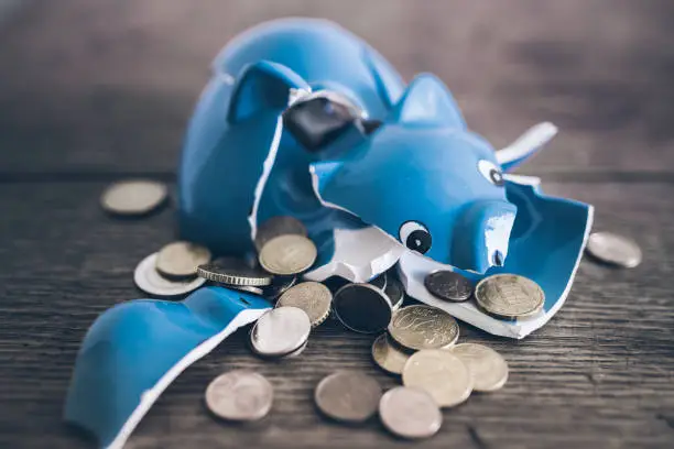 closeup of shattered broken piggy bank with coins on rustic wooden table