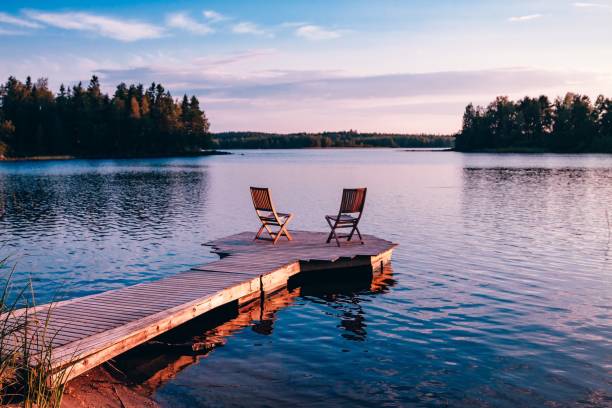 twee houten stoelen op een houten pier met uitzicht op een meer bij zonsondergang - huisje stockfoto's en -beelden