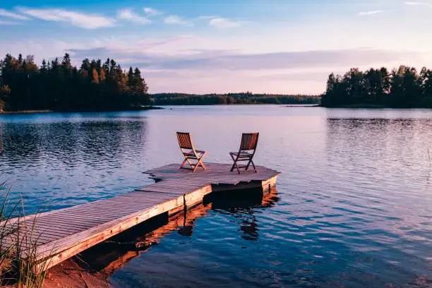 Photo of Two wooden chairs on a wood pier overlooking a lake at sunset