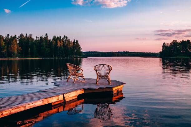 Two wooden chairs on a wood pier overlooking a lake at sunset stock photo