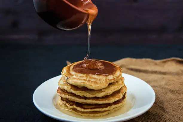 Pancakes pour honey from a bowl on a dark background Menu , restaurant recipe concept. Served in