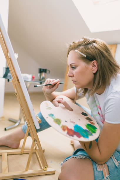 istock Happy young woman paints on canvas 955119730
