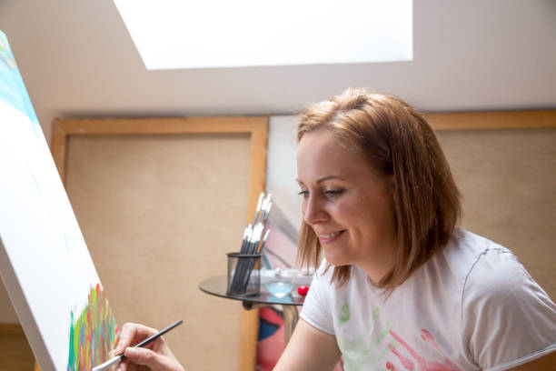 istock Happy young woman paints on canvas 955120282