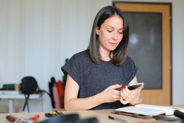 istock Girl creating handmade leather notebook and using smartphone for new ideas 955135624