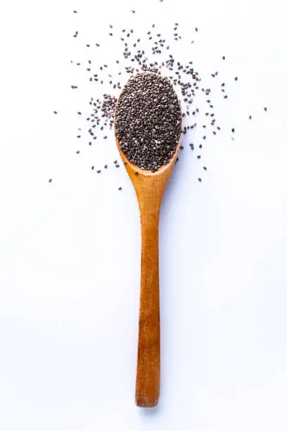 Flat lay of wooden spoon filled with small seeds of chia lying on white backgroun