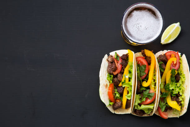 istock Corn tortillas with beef and vegetables, beer and lime on a black background, top view. Mexican kitchen. Copy space. Flat lay. 955140954