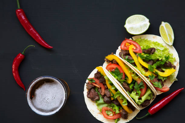 istock Tacos with beef and vegetables, beer and lime on a black background, top view. Mexican kitchen. Copy space. 955140992