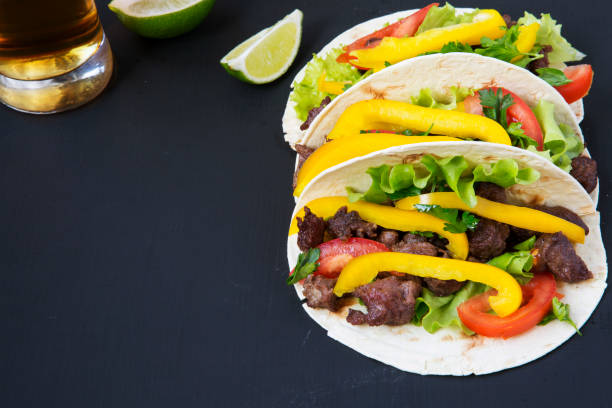 istock Tacos with beef and vegetables, beer and lime on a black background, side view. Closeup. 955140996