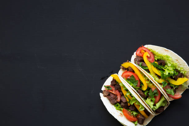 istock Corn tortillas with beef and vegetables on a black background, top view. Mexican kitchen. Copy space. Flat lay. 955144538