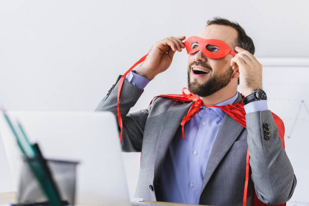 istock excited super businessman in cape looking through red mask in office 955152384