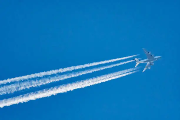 Looking up at a commercial passenger jumbo jet flying at a high altitude with the four turbine engines creating a vapor trail against the blue sky.