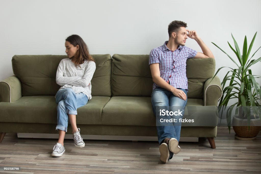 Couple sitting apart not talking because of quarrel Husband and wife sitting on different sides of couch not looking at each other and not talking, being in quarrel thinking about relationship problems, break up. Concept of family misunderstanding Couple - Relationship Stock Photo