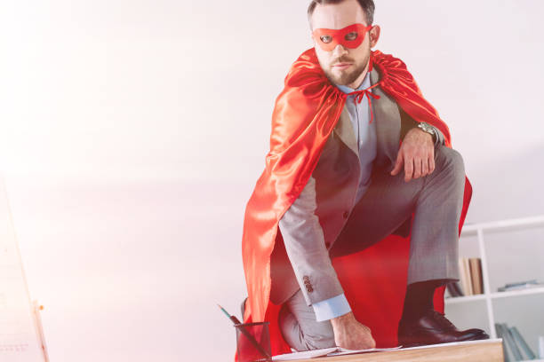istock handsome super businessman in mask and cape squatting on table in office 955166438