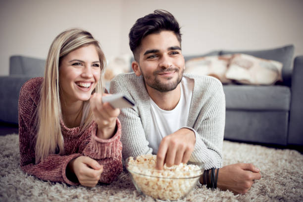 glückliches paar vor dem fernseher und essen popcorn - gamer watching tv adult couple stock-fotos und bilder