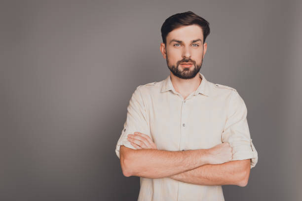istock Serious strict businessman with crossed hands on gray background 955172414