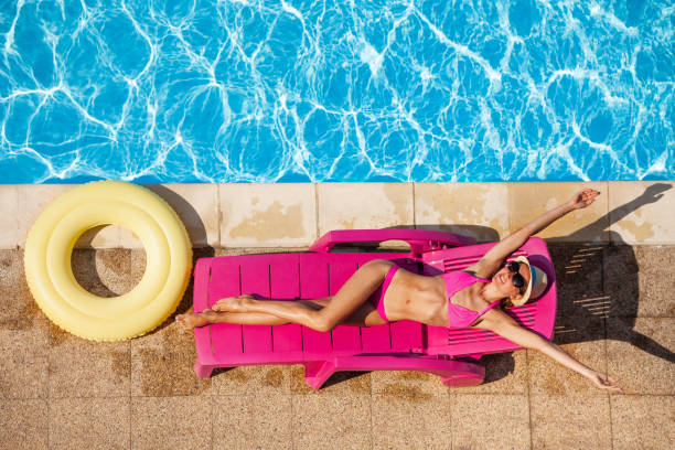 счастливая молодая женщина, отдыхая на шезлонге у бассейна - poolside enjoyment sensuality blue стоковые фото и изображения