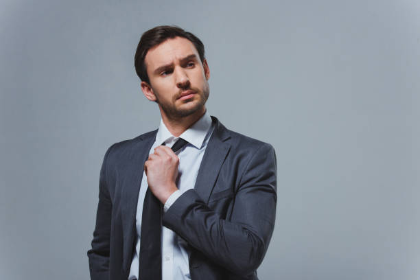 istock serious handsome businessman fixing tie isolated on grey 955175448