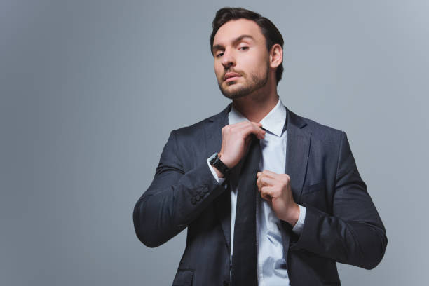 istock handsome businessman fixing tie and looking at camera isolated on grey 955175510