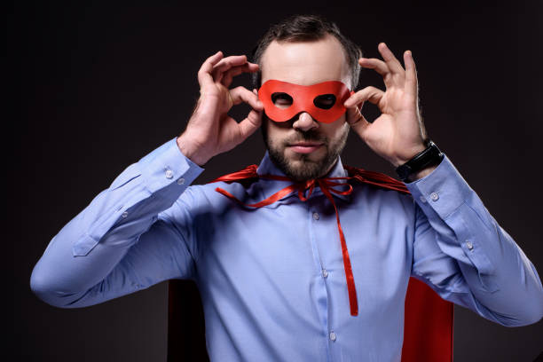 istock handsome super businessman in cape holding mask isolated on black 955175598